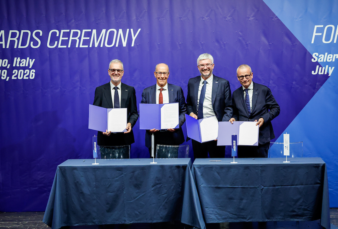 Four individuals stand at a table holding open blue folders during an awards ceremony in Salerno, Italy, on July 19, 2026.