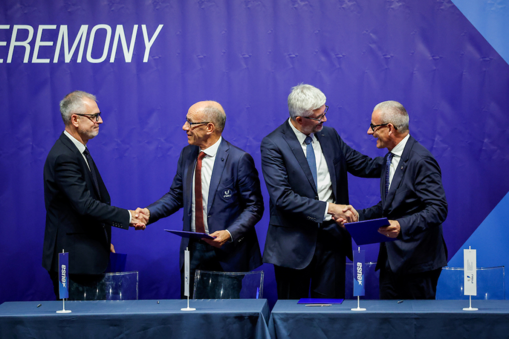 Four individuals in suits shake hands at a formal ceremony, standing before a blue backdrop with "CEREMONY" written on it.