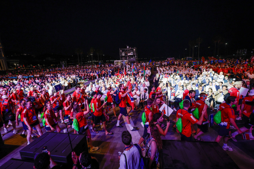 A large crowd of people, many wearing red and carrying Norwegian flags, gathers at night for a celebratory event.